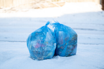 Two full blue plastic garbage bags placed on snow the roadside. Concept of recycling, public...