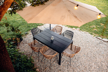 modern cozy backyard garden features a wooden table, chairs, and umbrella set amidst lush greenery on gravel, perfect for outdoor dining and relaxation