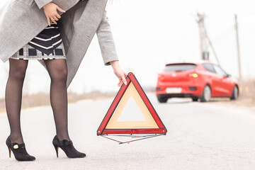 Young woman putting a triangle on a road. Car trouble concept