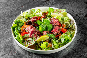 fresh salad with grilled meat, tomatoes, and mixed greens on a dark surface. The colorful ingredients create an appetizing and healthy meal option