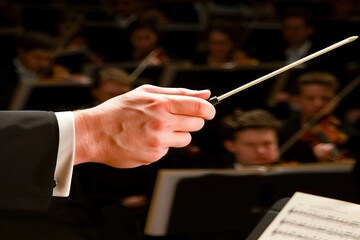 An orchestra conductor's hand holding the baton, with the symphony on stage in the background. Musical performance. Theater. Concert hall. Musicians. Command. Audience