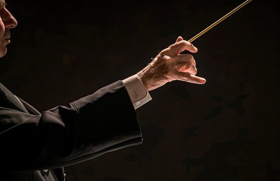 An orchestra conductor holding the baton against a dark background. Classical music. Gesture. Bandmaster. Wand. Concert hall, performance. Maestro. Band director, leader. Choir conductor. Pointing