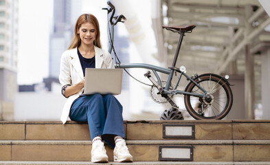 Confident businesswoman ride bicycle sit outside in downtown using computer. Environmentalist...