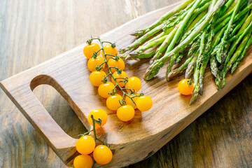 asparagus and a branch with yellow cherry tomatoes on a wooden board.