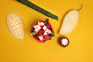 Beautiful Mangosteen mango dragon fruit cube fruit salad in dragon fruit skin bowl on yellow background green banana leaf