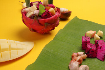 Beautiful Mangosteen mango dragon fruit cube fruit salad in dragon fruit skin bowl on yellow background green banana leaf