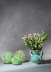 Foto op Aluminium A small bouquet of fresh spring flowers. Lilies of the valley in a light vase isolated on a gray background, green balls nearby. Lots of space for text. still life, postcard, gift © Alexander