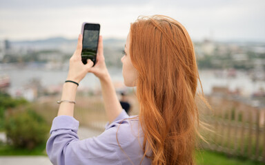 Young redhead girl taking photo of cityscape on sunny day. - 768634360