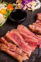 Tagliata di carne cotta al sangue sulla brace, scaloppata e servita in un piatto nero con contorno...