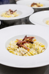 Fusilli con crema di formaggio e guarniti con pancetta croccante impiattati e pronti per essere serviti come prima portata di un evento