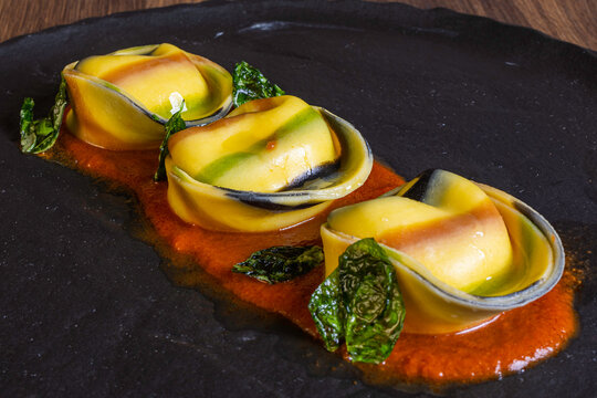 Cappellacci multicolor di pasta fatti a mano ripieni di stracciata di bufala e guarniti con sugo di pomodoro e basilico fritto serviti in un ristorante come primo piatto