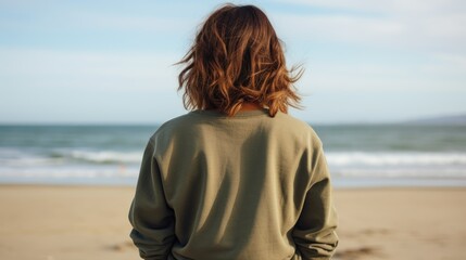 Back view of a girl with wavy brown hair in plain olive crewneck sweatshirt mockup on a beach background with the ocean