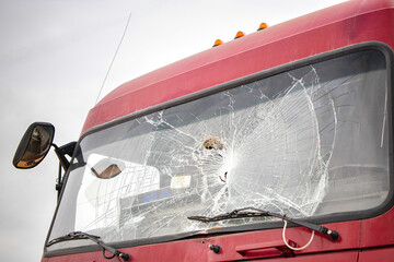 The windshield of a red truck is shattered, showing signs of impact and damage