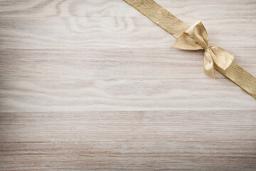 Shiny golden bow in upper right corner on wooden background