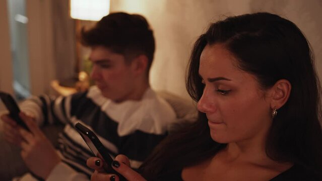 Young couple sitting on the sofa using smart phones in a warm cosy home