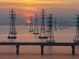 High-voltage transmission tower, cars moving on the highway, and sunset scenery
