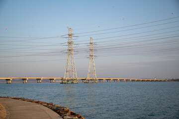 A view of a bridge over the sea and a high-voltage electric transmission tower
