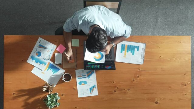 Top aerial view of manager working on laptop while looking at data analysis. Leader compare financial statistic graph while making decision at meeting table with document scatter around. Convocation.