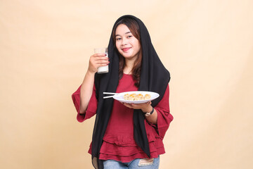 Beautiful elegant Asian woman in a red shirt wearing a hijab smiles holding a glass of milk and carrying a plate containing dimsum (Chinese food). used for food, beverage and culinary content