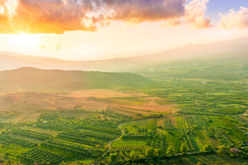 scenic rustic landscape with green hills and farms in a mountain valley during colorful cloudy sunset
