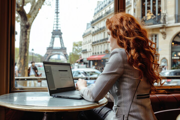 A young woman is sitting in a cafe near the Eiffel tower and working on a laptop
