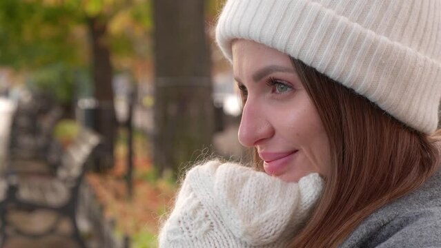 Cute woman in warm white hat and mittens in autumn park, closeup
