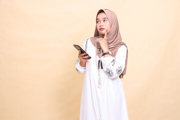 a young indonesia Muslim woman wearing a hijab thinks hard holding prayer beads and WhatsApp via smartphone gadget. for advertising, lifestyle, banners and Ramadan