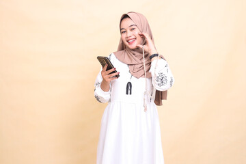 a young Asian Muslim girl wearing a hijab smiles in love holding prayer beads and chatting via smartphone gadget. for advertising, lifestyle, banners and Ramadan