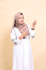 Beautiful young indonesian Muslim woman wearing a hijab carrying left-sided prayer beads with a graceful smile looking at her while promoting a product. for advertising, content, banners and Ramadan