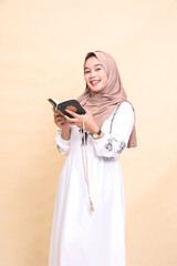 beautiful indonesia Muslim mature woman in hijab candid smiling at the camera holding prayer beads while reading the quran. for advertising, lifestyle, banners and Ramadan