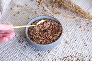 Golden teaspoon of flax seeds in a bowl and dried flax flowers on a cotton napkin background....