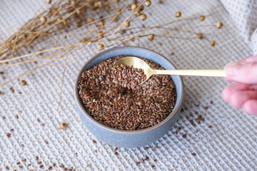 Golden teaspoon of flax seeds in a bowl and dried flax flowers on a cotton napkin background. Organic food, veganism, vitamins, health.