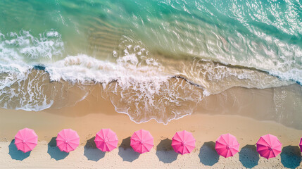 Fototapeta premium Beach with pink umbrellas, top view, drone photo, sea waves in the background, summer vacation concept