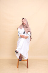 full body portrait of a young indonesia Muslim woman wearing an elegant hijab sitting in a chair holding her knees. for advertising, lifestyle, banners and Ramadan