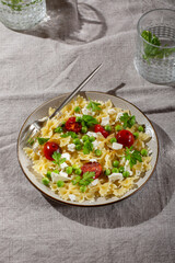 Farfalle pasta with  green peas, tomatoes and soft cheese on gray table. Vegetarian food.