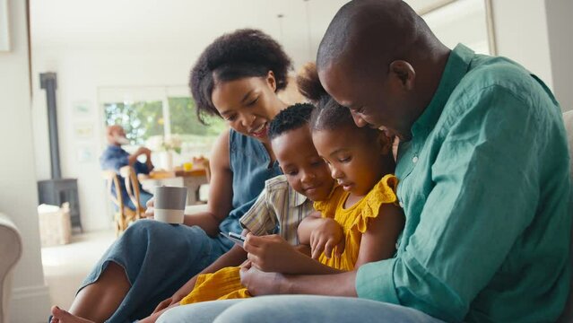 Family indoors at home sitting on sofa with digital tablet playing game with grandparents in background - shot in slow motion