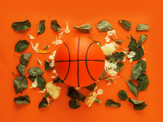 Classic basketball on orange color surface with green rose leaf and petals, love sport concept. Flat lay.