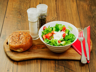 Serving of a fresh green salad with lettuce, tomato, cucumber and olive oil on a wooden board and...