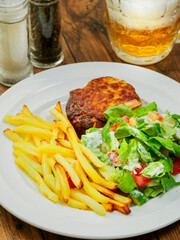 Burger with melted cheese toping, fresh green salad with lettuce and tomato and cucumber and fired potato chips on a wooden table. Tasty dinner. High quality product meal. Close up.