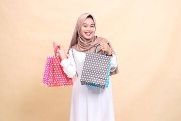 the charm of a young Asian Muslim woman wearing a hijab with a cheerful smile looking at the front carrying colorful paperbags with variations up and down. for advertising, banners and Ramadan