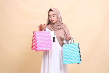 the charm of a young Muslim woman wearing a hijab, sullenly looking at and carrying the contents of a colorful paper bag from top-down shopping. for advertising, lifestyle, banners and Ramadan