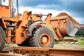 A large orange tractor or a loader is parked on top of a train track, blocking the path for any approaching trains