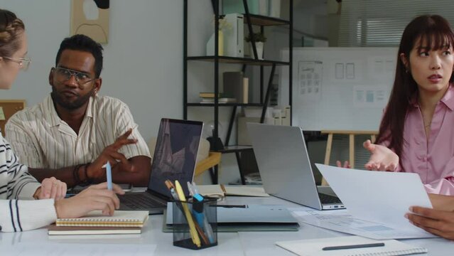 Pan shot of team of multiethnic young developers discussing app launch in modern office