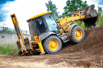 A big yellow loader is seen driving down a dusty dirt road, kicking up clouds of dust as it moves along