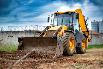 A bulldozer or a loader is actively digging dirt in front of a sturdy barbed wire fence, showcasing...