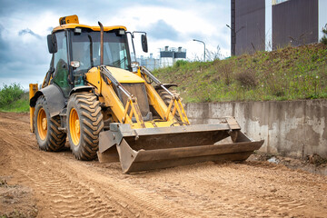 A tractor or a loader is parked on a dirt road, surrounded by fields and greenery under a clear sky