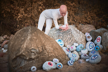 Young hairless girl with alopecia in white futuristic costume pensively examines stone with eye at surreal landscape, symbolizes introspection and reevaluation of individuality