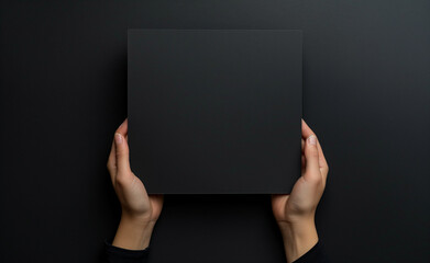 Hands are holding a black sheet of paper with a black background. - 768695332