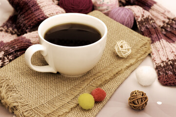 Cup of coffee on burlap close-up. Hot coffee and a warm knitted scarf for a cozy atmosphere.