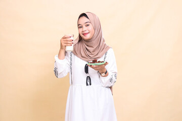 a beautiful Asian Muslim woman wearing a hijab smiles carrying a glass of milk and dates to break the fast. used for advertising, health, Eid and Ramadan